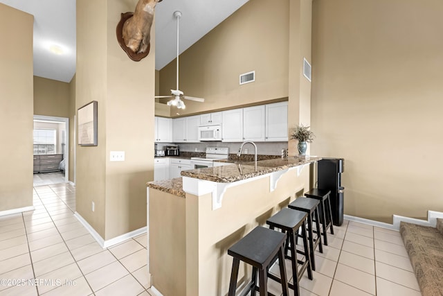 kitchen featuring white appliances, light tile patterned floors, visible vents, dark stone countertops, and a peninsula