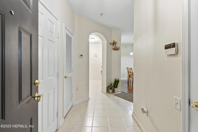 corridor with arched walkways, baseboards, and light tile patterned floors