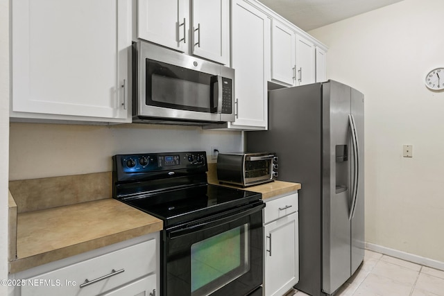 kitchen with a toaster, light countertops, appliances with stainless steel finishes, white cabinetry, and baseboards