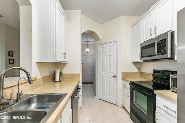 kitchen featuring arched walkways, stainless steel appliances, light countertops, white cabinets, and a sink