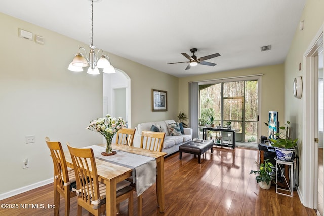 dining space with baseboards, visible vents, arched walkways, dark wood-type flooring, and ceiling fan with notable chandelier