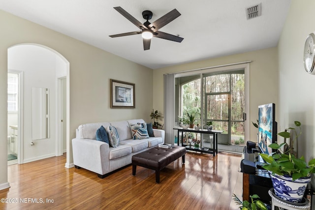 living room featuring baseboards, visible vents, a ceiling fan, arched walkways, and wood finished floors