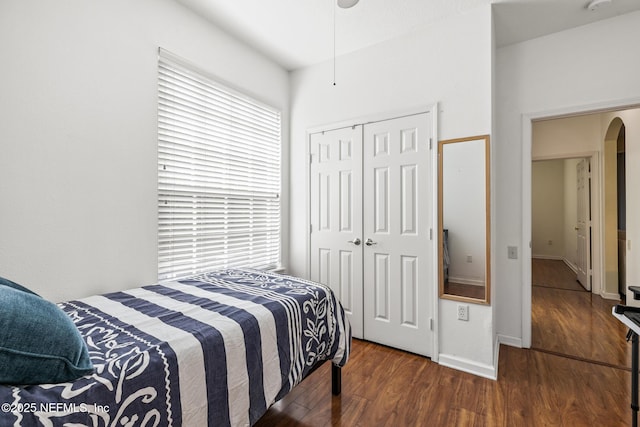 bedroom with arched walkways, a closet, wood finished floors, and baseboards