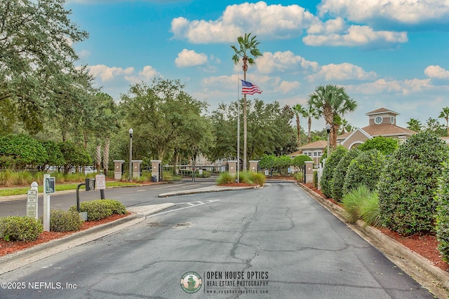 view of road featuring street lights, curbs, a gated entry, and a gate