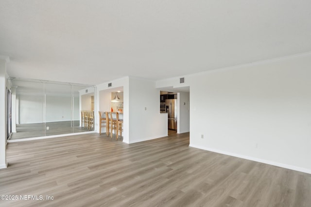 unfurnished living room featuring ornamental molding, light wood finished floors, visible vents, and baseboards