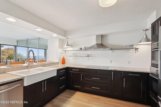 kitchen with open shelves, appliances with stainless steel finishes, a sink, light wood-type flooring, and wall chimney exhaust hood