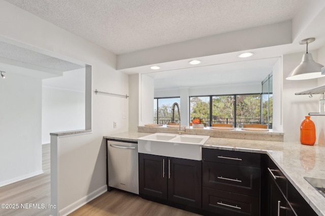 kitchen featuring stainless steel dishwasher, light wood-style floors, a sink, a textured ceiling, and dark cabinetry