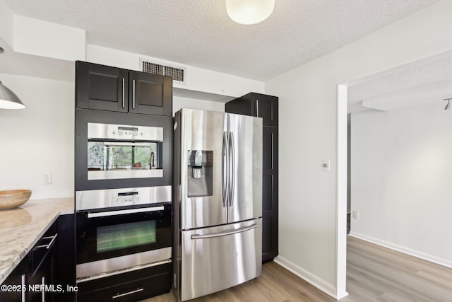 kitchen with visible vents, light wood-style flooring, appliances with stainless steel finishes, a textured ceiling, and dark cabinets