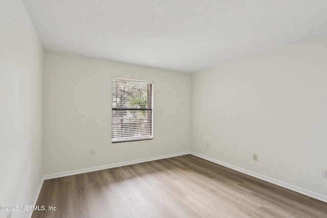 empty room featuring a textured ceiling, wood finished floors, and baseboards