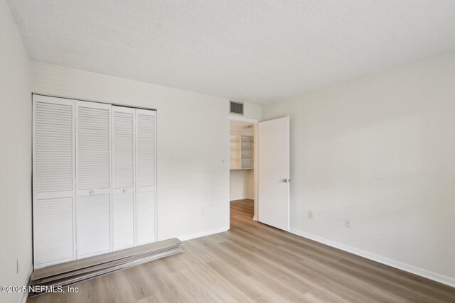 unfurnished bedroom featuring a closet, visible vents, baseboards, and wood finished floors