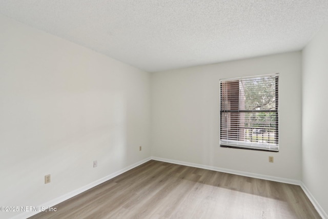 empty room with a textured ceiling, wood finished floors, and baseboards