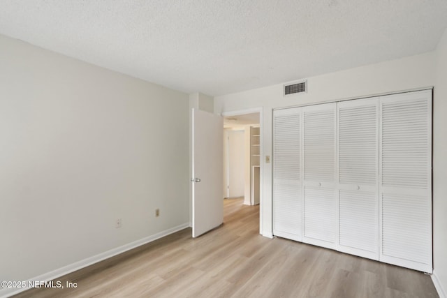 unfurnished bedroom with a textured ceiling, light wood-type flooring, visible vents, and baseboards