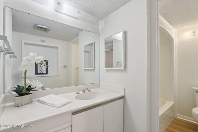 full bathroom with a textured ceiling, toilet, wood finished floors, vanity, and a bathtub