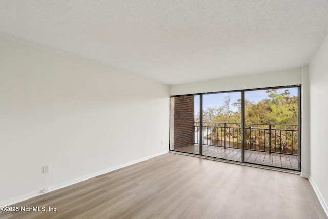 unfurnished room with a textured ceiling, wood finished floors, and baseboards