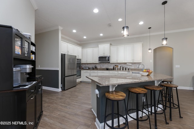 kitchen featuring wood finished floors, appliances with stainless steel finishes, a kitchen bar, and backsplash