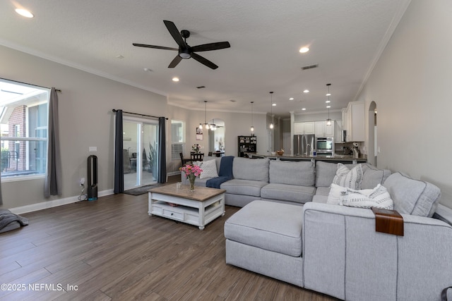 living area featuring arched walkways, dark wood finished floors, visible vents, ornamental molding, and baseboards