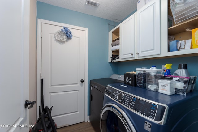 washroom with a textured ceiling, washing machine and dryer, dark wood-type flooring, visible vents, and cabinet space