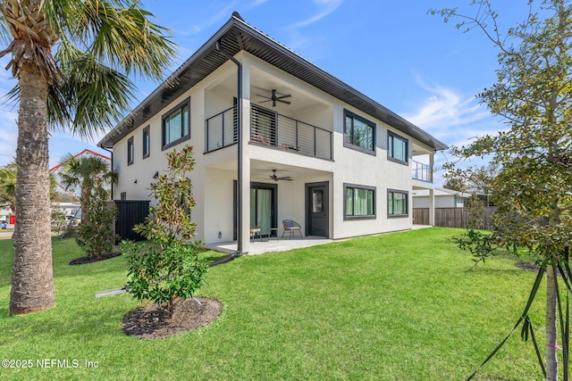 back of house featuring a balcony, fence, a ceiling fan, and a yard