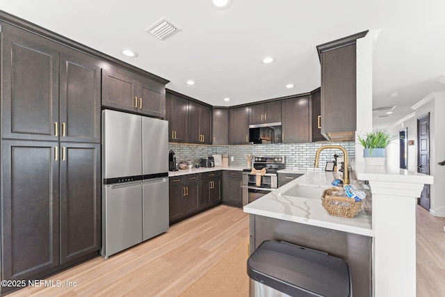 kitchen with light stone counters, stainless steel appliances, a sink, dark brown cabinets, and tasteful backsplash