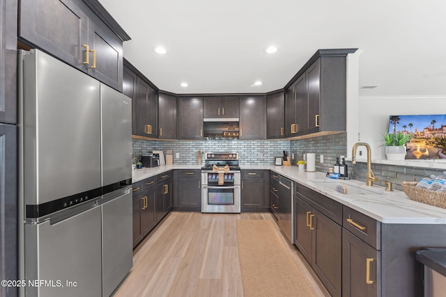 kitchen featuring stainless steel appliances, a sink, light wood-type flooring, light stone countertops, and tasteful backsplash