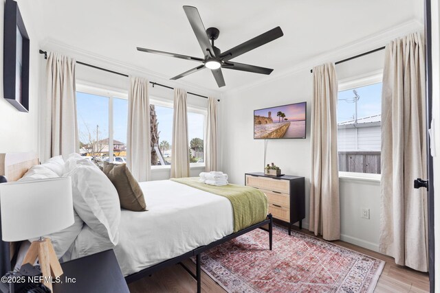 bedroom featuring light wood-type flooring, multiple windows, baseboards, and crown molding