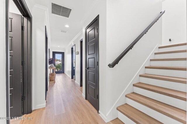 hall featuring visible vents, baseboards, light wood-style floors, ornamental molding, and stairway