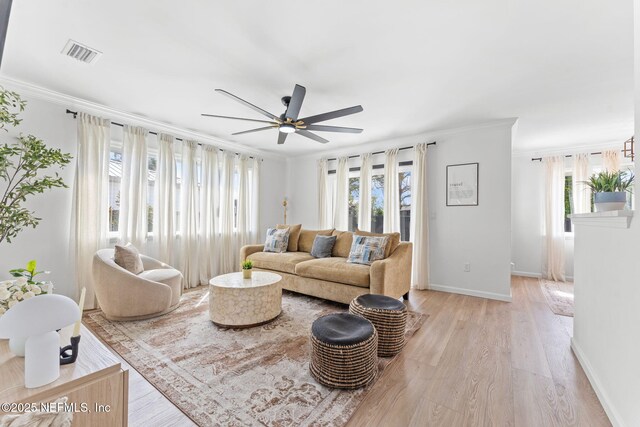 living room with visible vents, baseboards, light wood-style flooring, ceiling fan, and ornamental molding