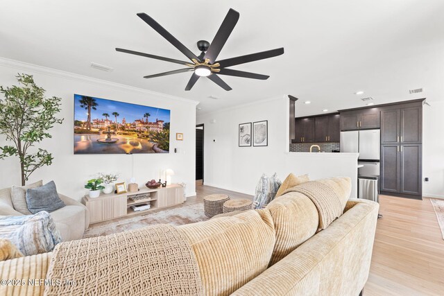 living area featuring light wood finished floors, visible vents, and crown molding