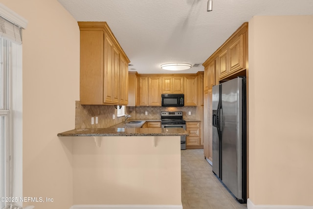 kitchen featuring decorative backsplash, dark stone countertops, a peninsula, stainless steel appliances, and a sink