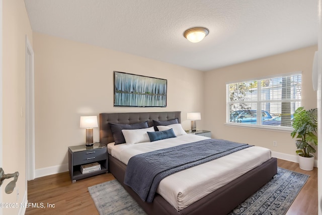 bedroom with a textured ceiling, baseboards, and wood finished floors