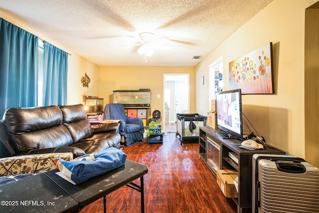 living room with ceiling fan, visible vents, dark wood finished floors, and a textured ceiling