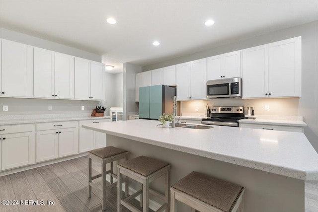 kitchen featuring a kitchen island with sink, appliances with stainless steel finishes, white cabinets, and a breakfast bar area