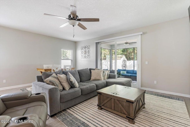 living area with baseboards, ceiling fan, a textured ceiling, and light wood finished floors