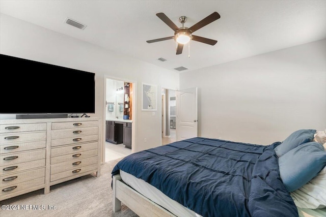 bedroom with a ceiling fan, light colored carpet, visible vents, and ensuite bath