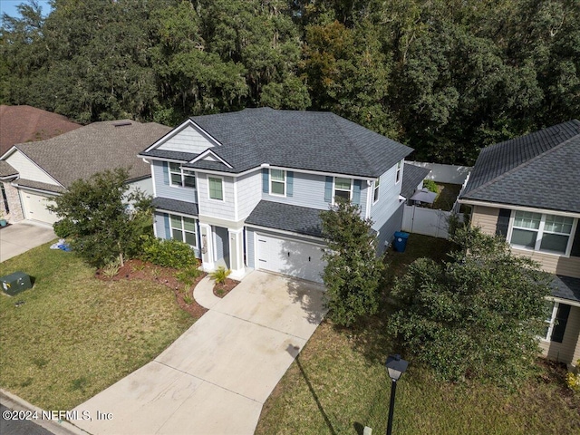 traditional-style house featuring a garage, a shingled roof, concrete driveway, fence, and a front lawn