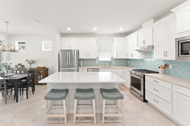 kitchen featuring visible vents, appliances with stainless steel finishes, a breakfast bar, under cabinet range hood, and a sink