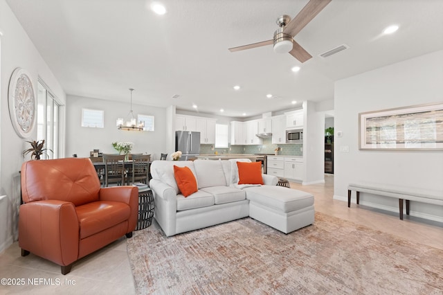 living area featuring plenty of natural light, ceiling fan with notable chandelier, visible vents, and light tile patterned flooring