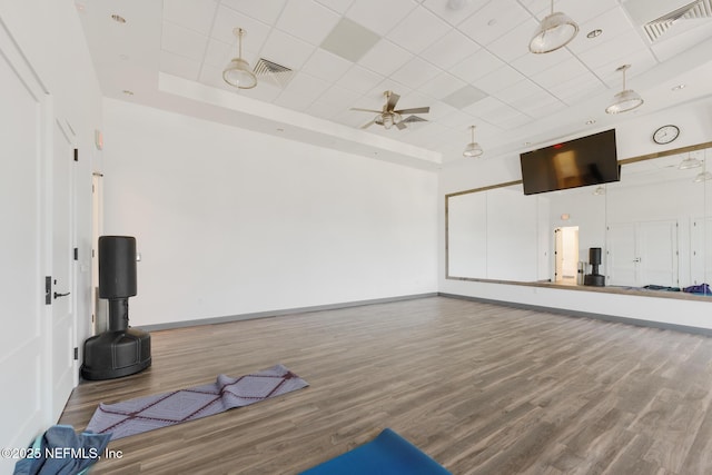 workout area with baseboards, visible vents, a raised ceiling, and wood finished floors