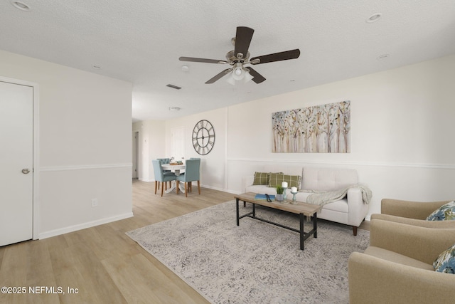 living room featuring baseboards, visible vents, ceiling fan, wood finished floors, and a textured ceiling