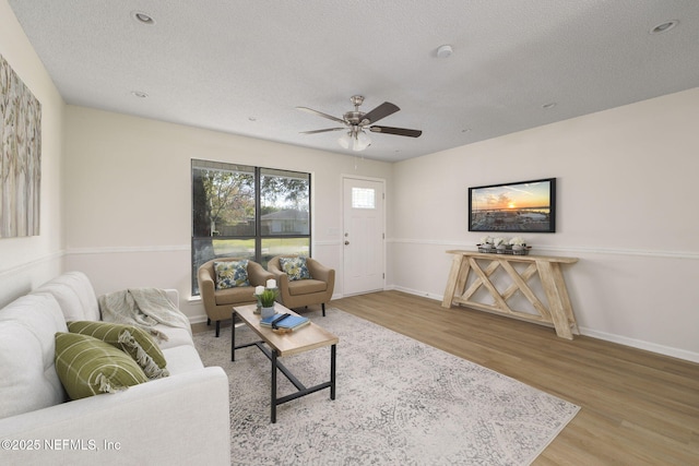 living area featuring a ceiling fan, a textured ceiling, baseboards, and wood finished floors