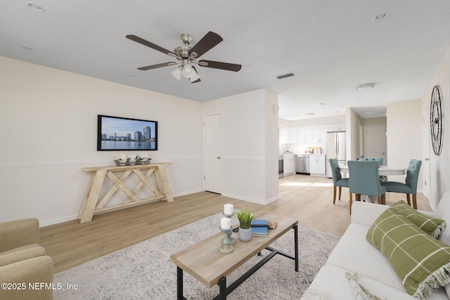 living area featuring a textured ceiling, baseboards, visible vents, and light wood-style floors