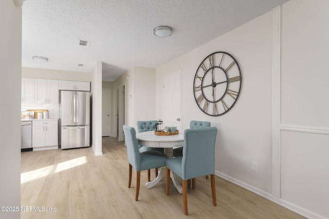 dining room featuring baseboards, light wood-style flooring, visible vents, and a textured ceiling