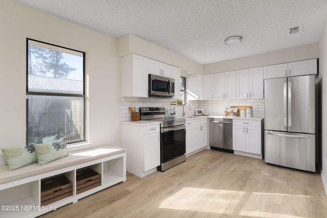 kitchen featuring visible vents, white cabinets, light wood-style floors, appliances with stainless steel finishes, and decorative backsplash