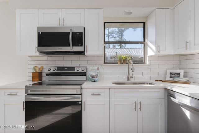 kitchen featuring stainless steel appliances, light countertops, decorative backsplash, white cabinets, and a sink