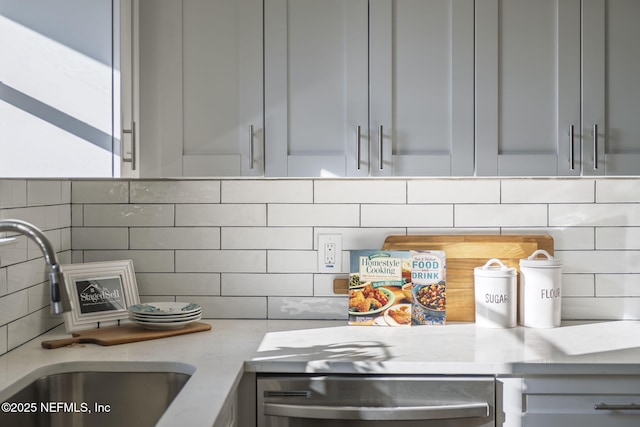 kitchen with light stone countertops, gray cabinetry, a sink, decorative backsplash, and dishwasher