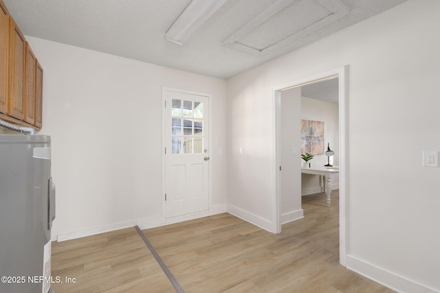 interior space with a textured ceiling, electric water heater, baseboards, light wood-style floors, and attic access