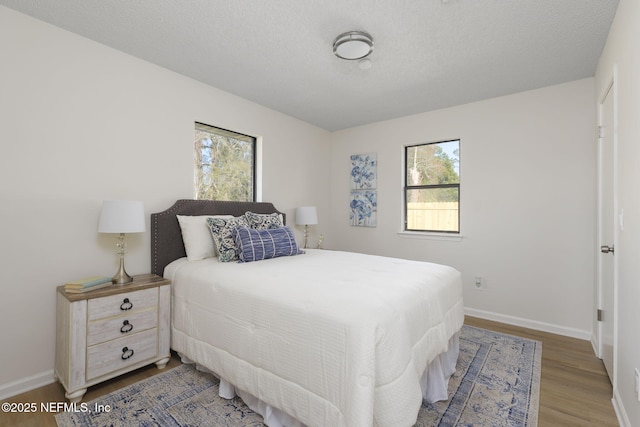 bedroom with a textured ceiling, wood finished floors, and baseboards