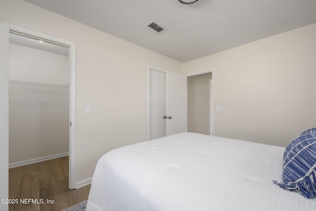 bedroom with visible vents, wood finished floors, a walk in closet, a textured ceiling, and a closet