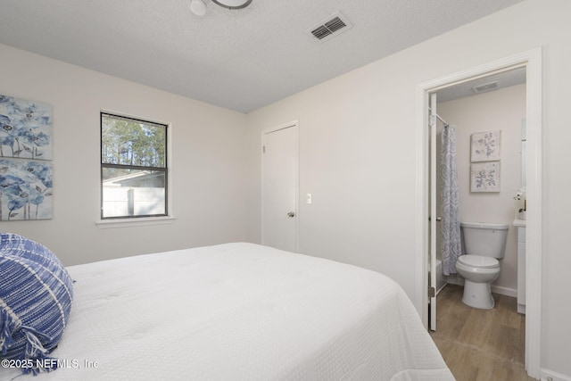 bedroom featuring a textured ceiling, light wood finished floors, connected bathroom, and visible vents