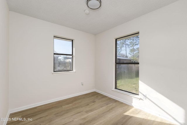 spare room with a textured ceiling, baseboards, a wealth of natural light, and wood finished floors